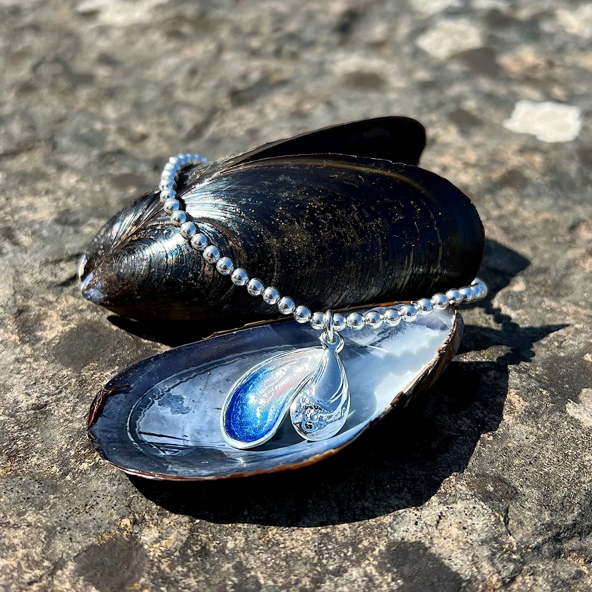 A silver beaded bracelet with a drop pendant in the shape of mussels in blue enamel lifestyle image