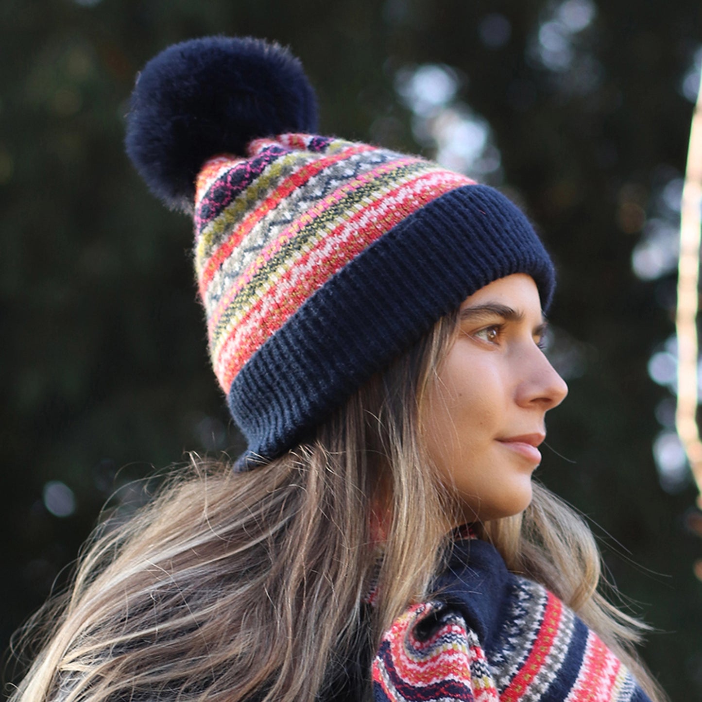 Model wearing knitted Nordic stripe pattern hat in blue, green and rust colours with faux fur pompom