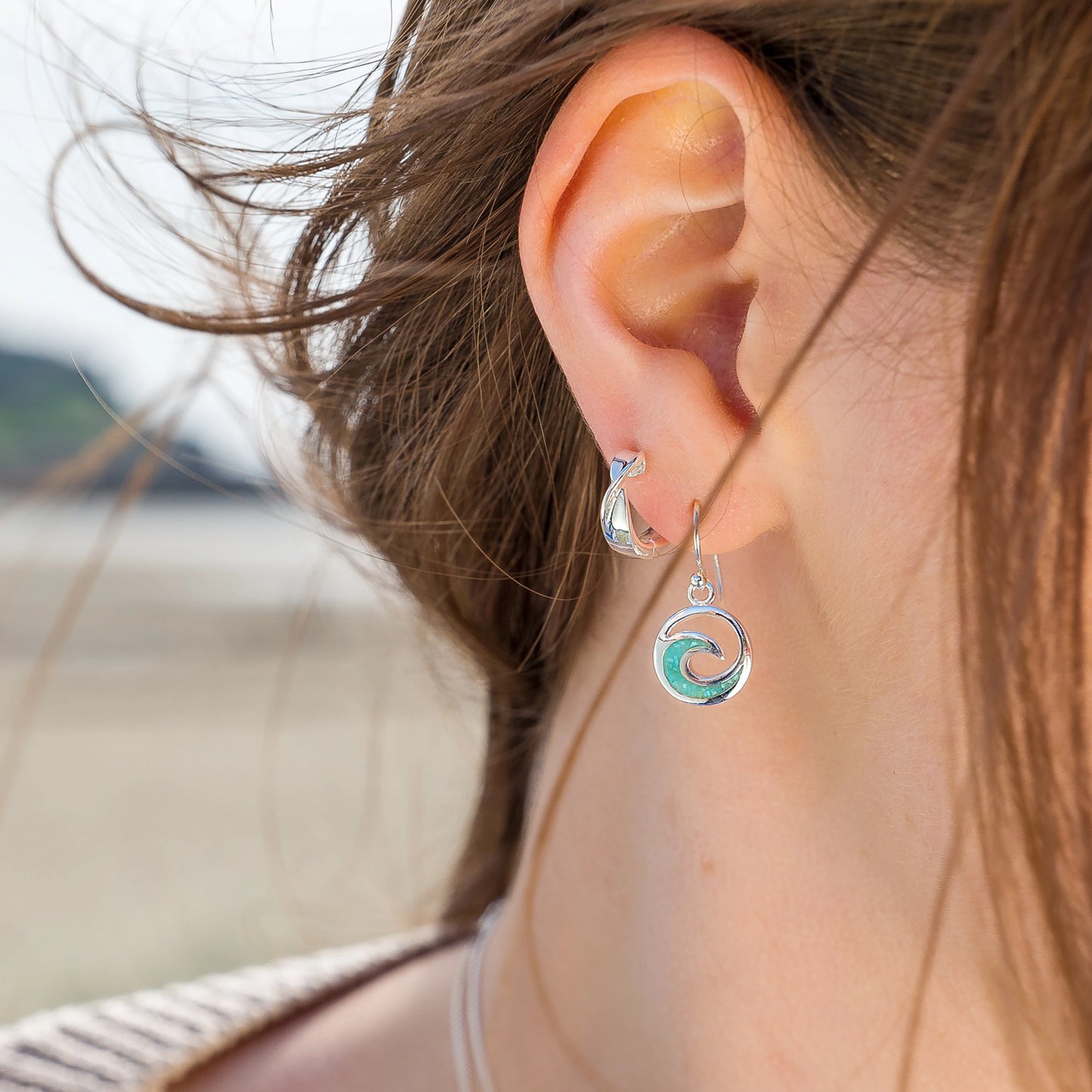 Model wearing round drop earrings with turquoise ocean wave design