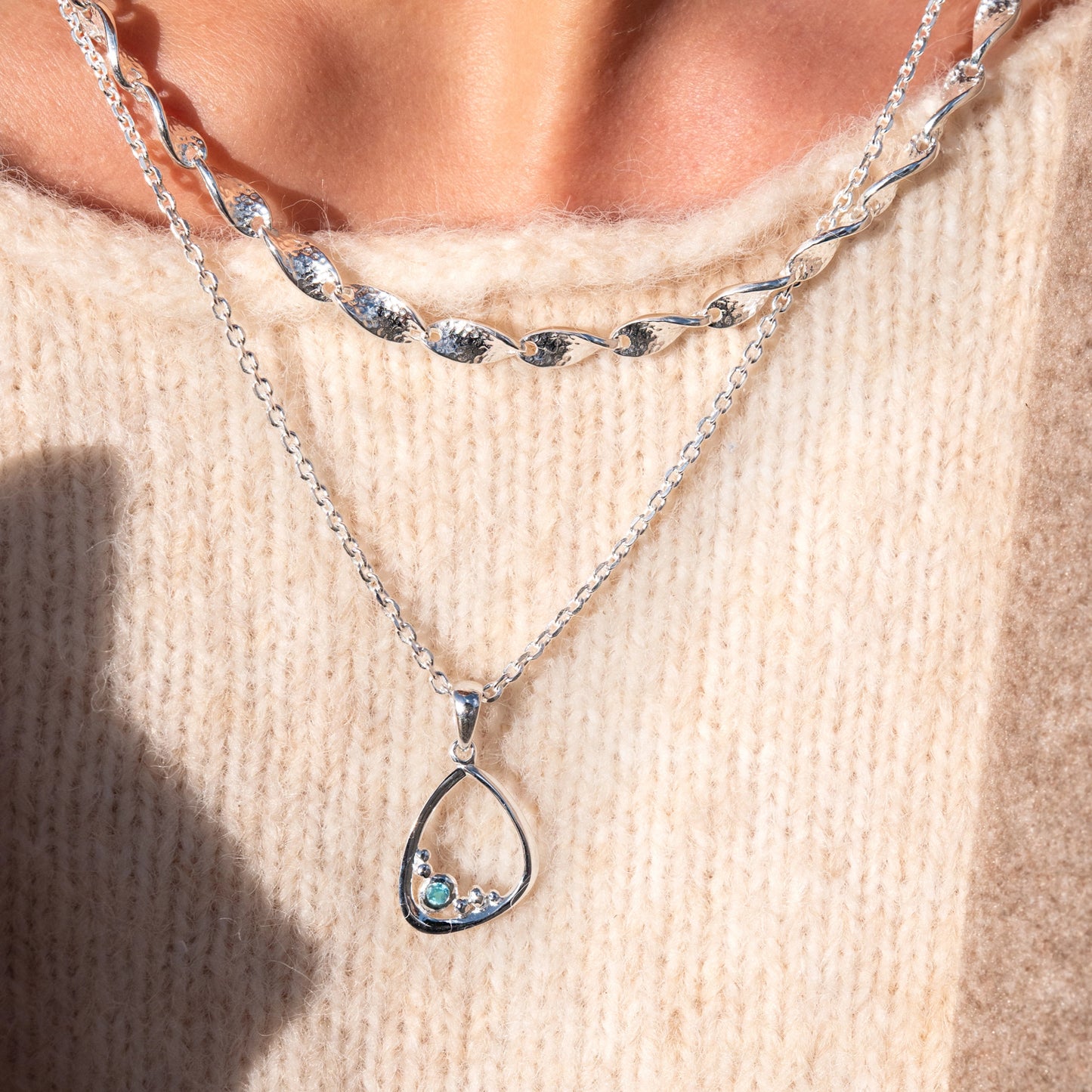 Open frame pendant with small stone shapes and blue topaz stone inspired by coastal coves model