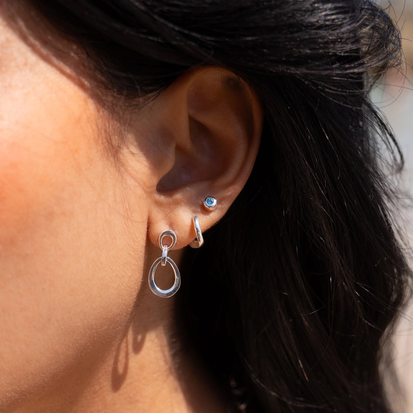Model wearing drop earrings with three linked organic oval shapes in sterling silver