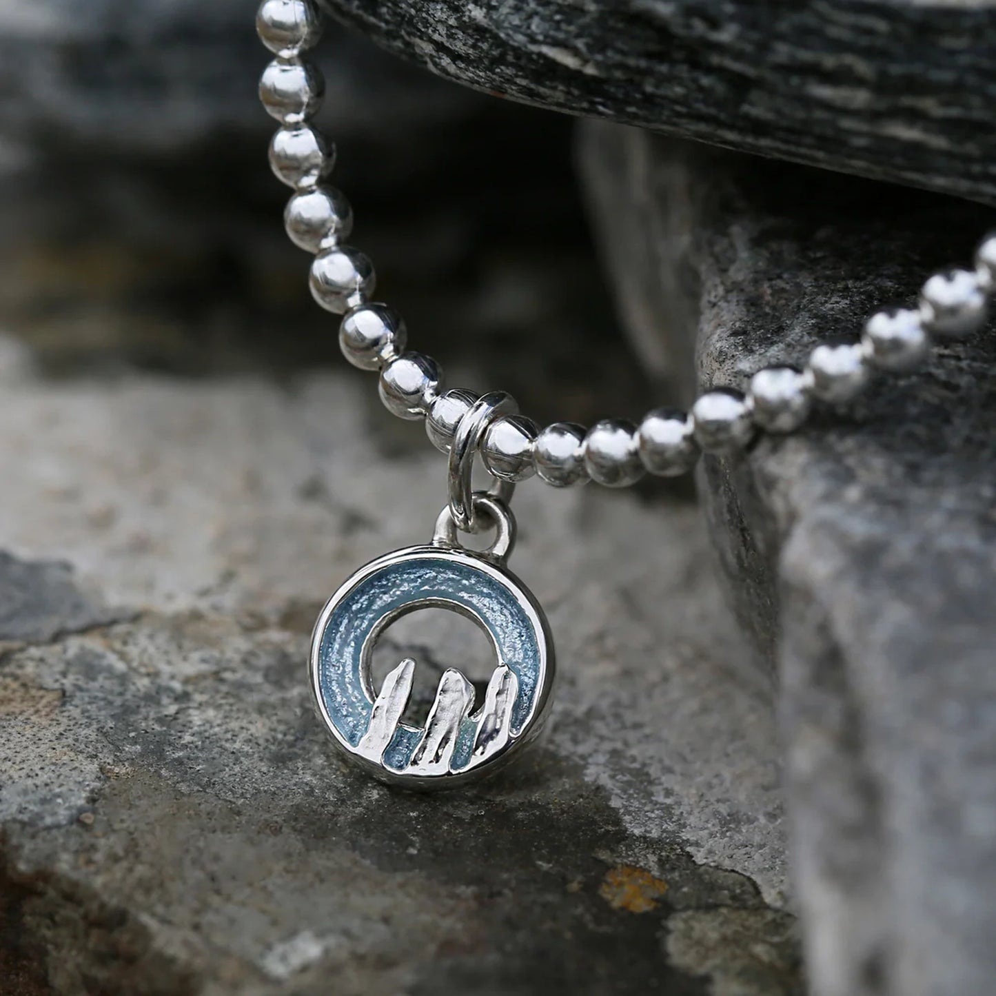 Silver stretch bracelet with a round blue grey enamelled charm with standing stone design - lifestyle