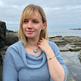 Model wearing silver bracelet with wavey silver bars, round ocean wave pendants with blue enamel and a matching necklet