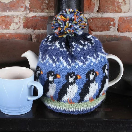 A knitted tea cosy with a pompom and a row of puffins design with beaded eyes lifestyle