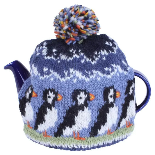 A knitted tea cosy with a pompom and a row of puffins design with beaded eyes on teapot