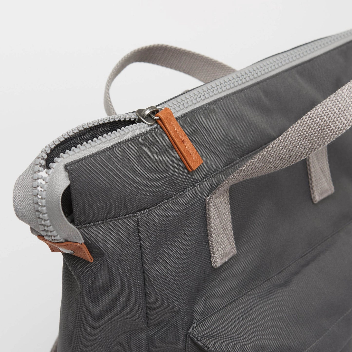 Close up of a chunky zipper with brown leatherette pull on dark grey backpack