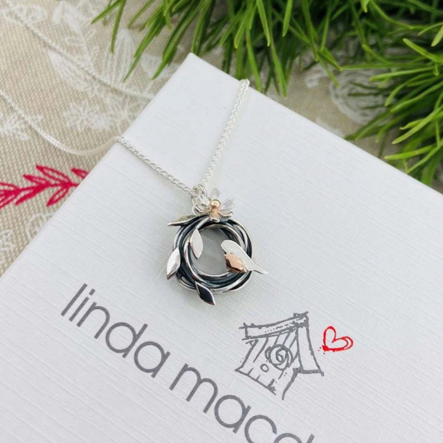 A silver bird nest shaped pendant with a little robin featuring a rose gold breast on box