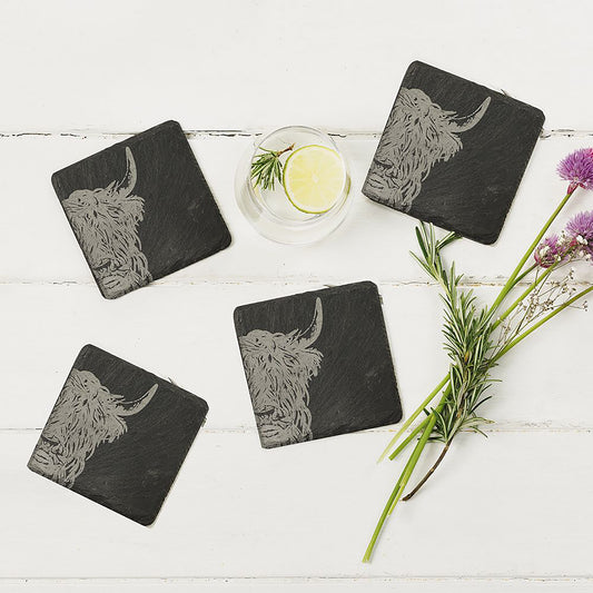 4 square slate coasters with engraved Highland cow on each staged on a table 