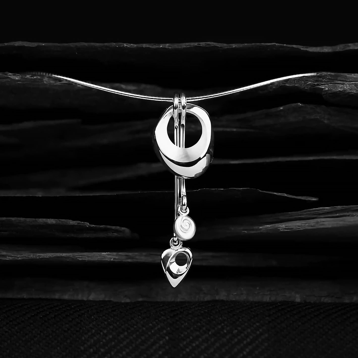 Detail of a silver necklet featuring an abstract contemporary pendant with swirl and arrow drops