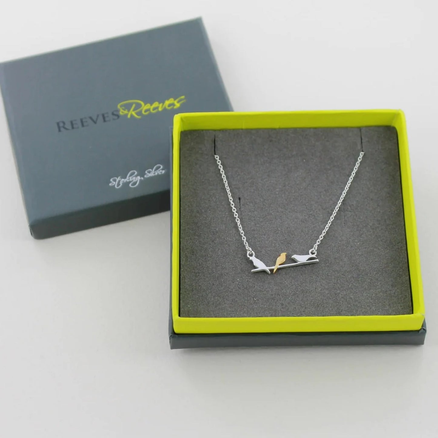 A necklace featuring three birds on a branch in silver, the centre one in gold in a box