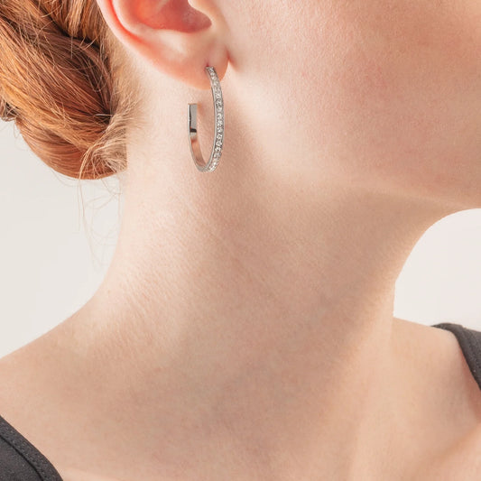 Model wearing a pair of silver hoop earrings set with white rhinestones