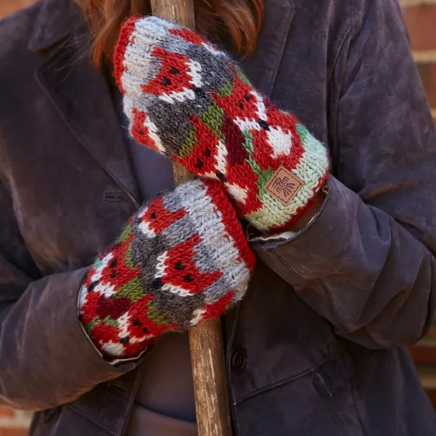 A pair of knitted handwarmers in green featuring rows of orange foxes on model