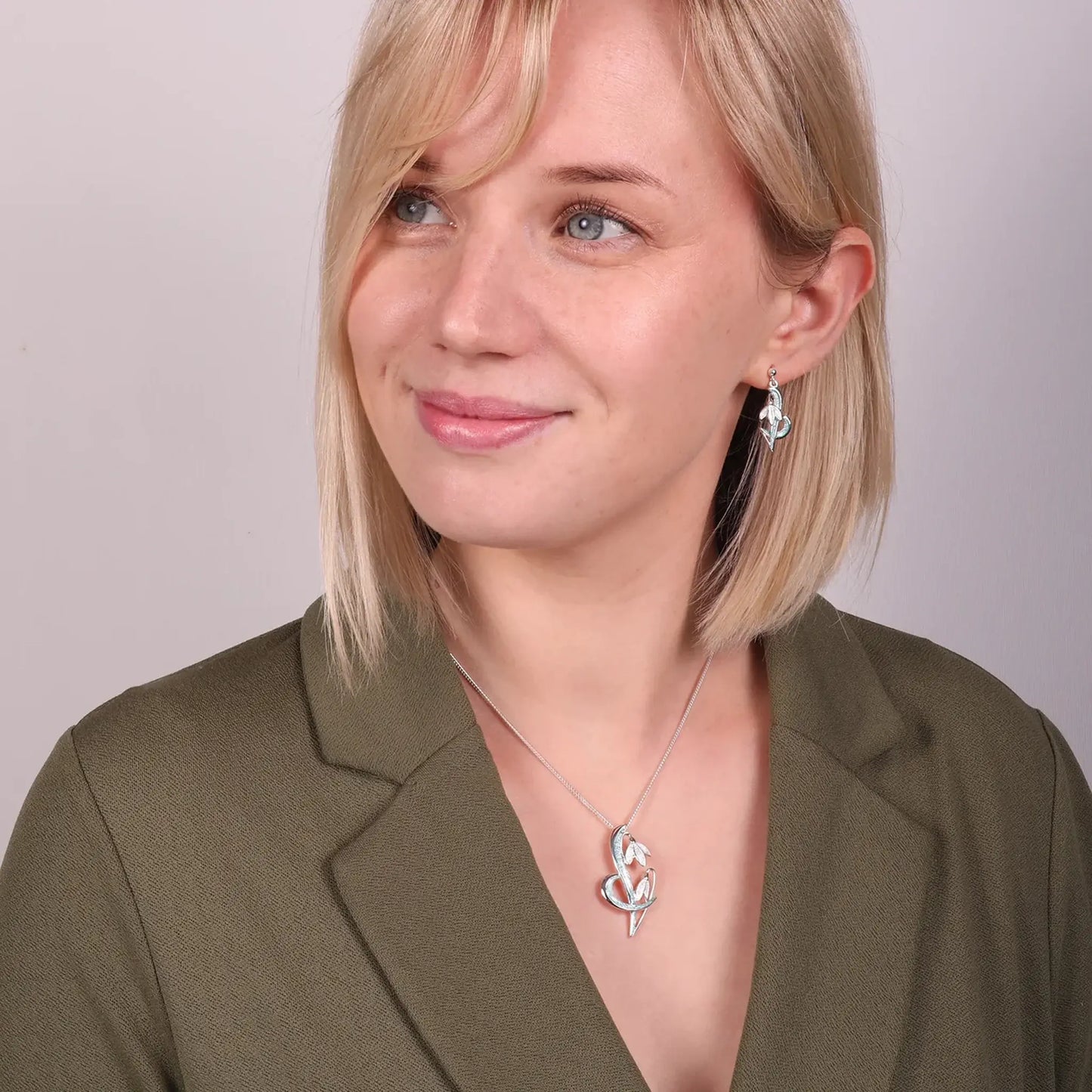 Model wearing silver snowdrop drop earrings and pendant in green and white enamel