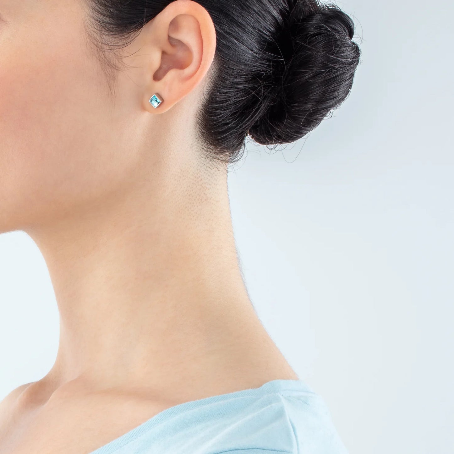 Model wearing a pair of square silver stud earrings featuring an aqua crystal stone