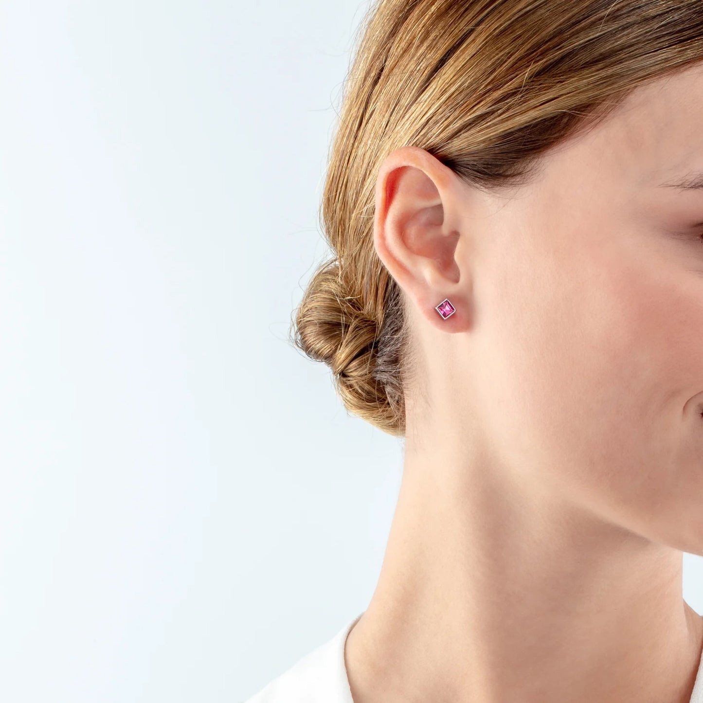 Model wearing a pair of square steel stud earrings featuring a pink crystal stone