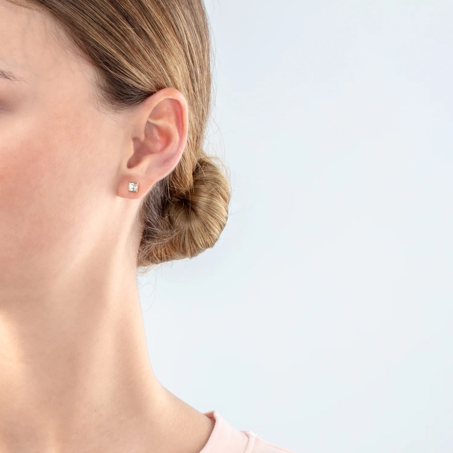 Model wearing a pair of square gold stud earrings featuring an white crystal stone