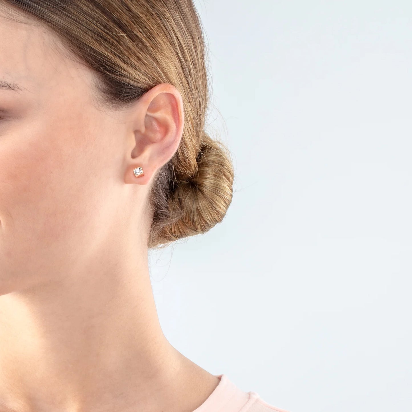 Model wearing a pair of square rose gold stud earrings featuring an white crystal stone