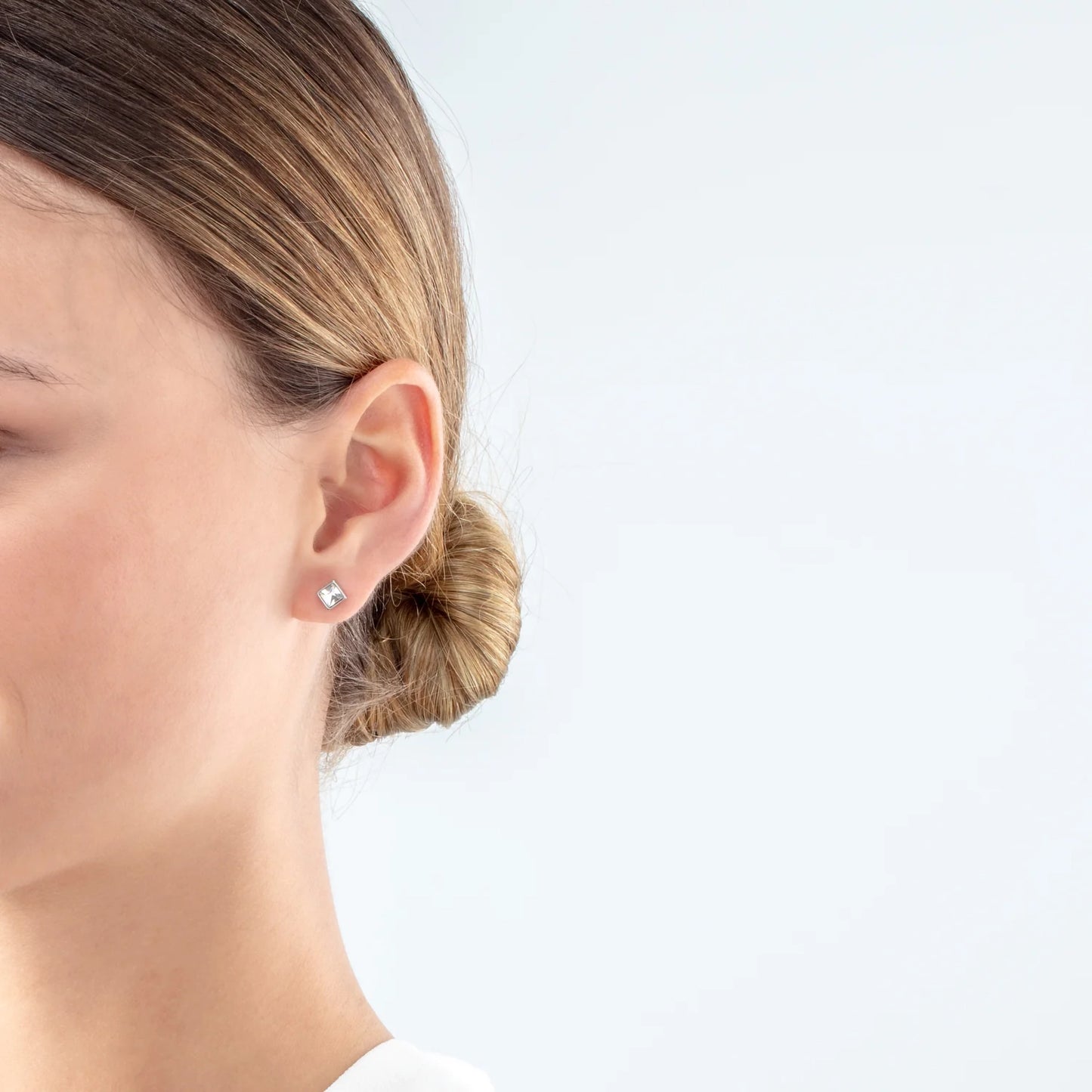 Model wearing a pair of square steel stud earrings featuring an white crystal stone