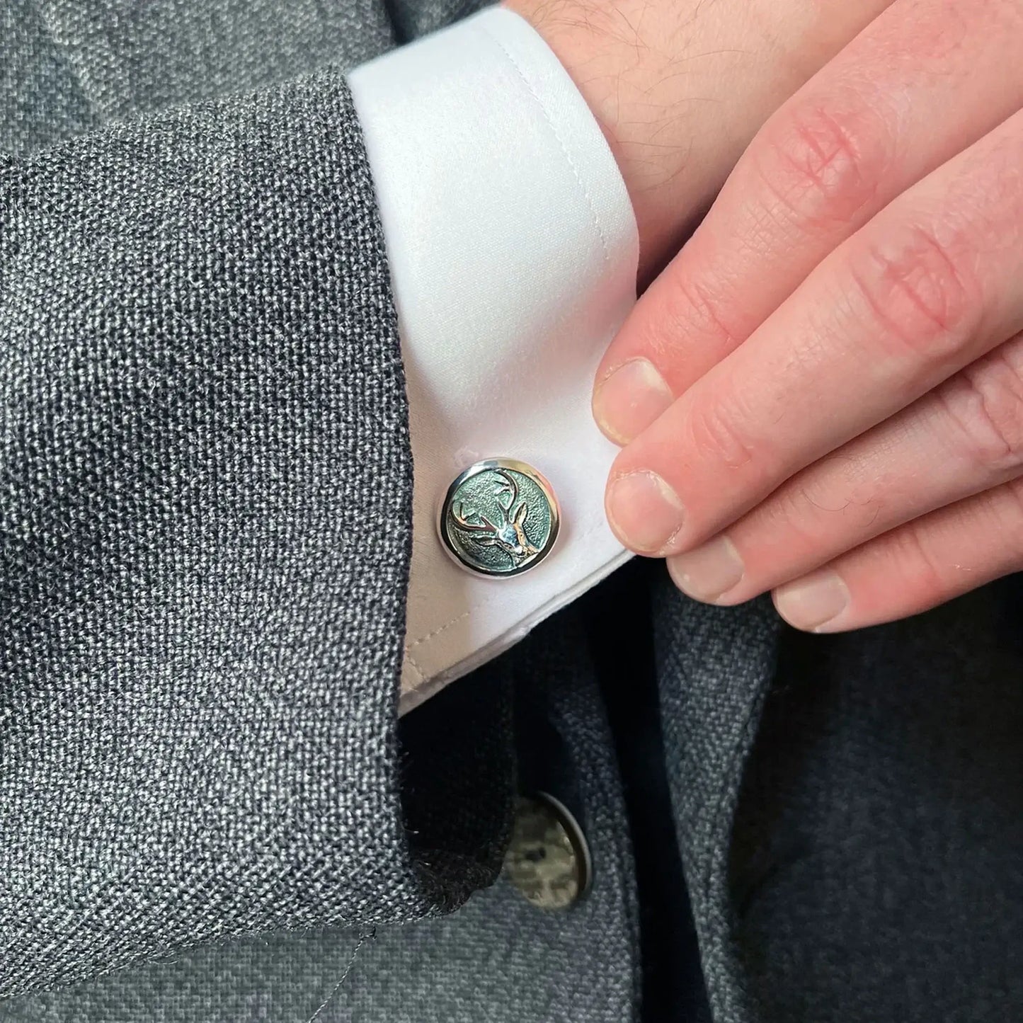 Model wearing round silver cufflinks with stag's head design in moss green enamel