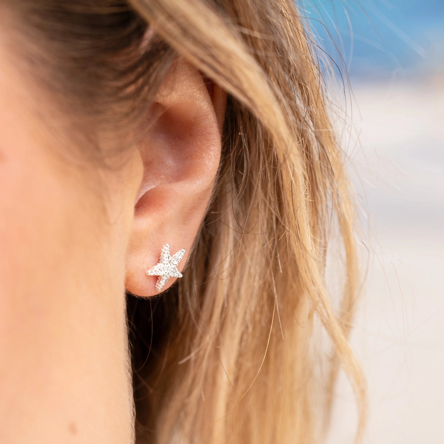 Model wearing silver stud earrings shaped like starfish with a heavily textured finish