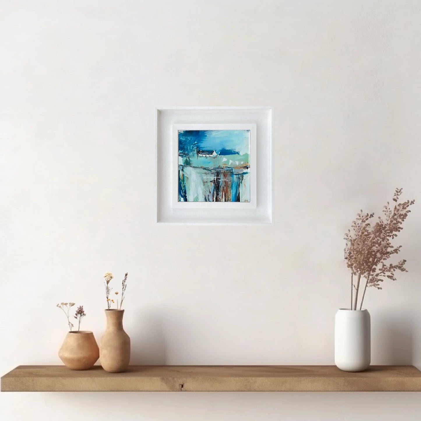 White framed art tile featuring a small white bothy in a vibrant blue setting hanging