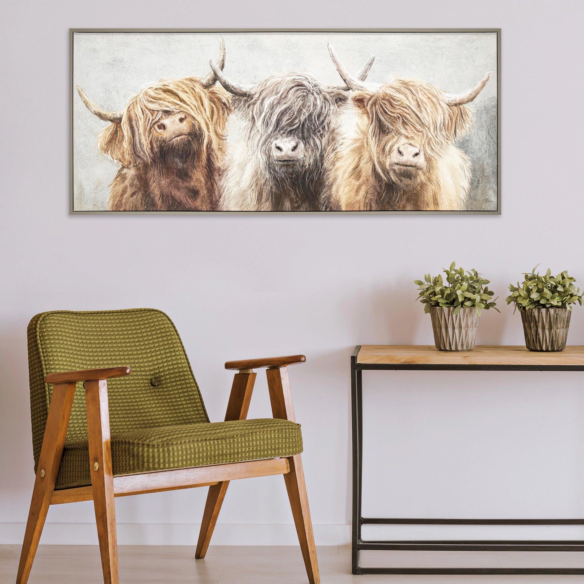 Long framed canvas of three Highland cows with an impressionist grey background of foliage hanging in a light room.