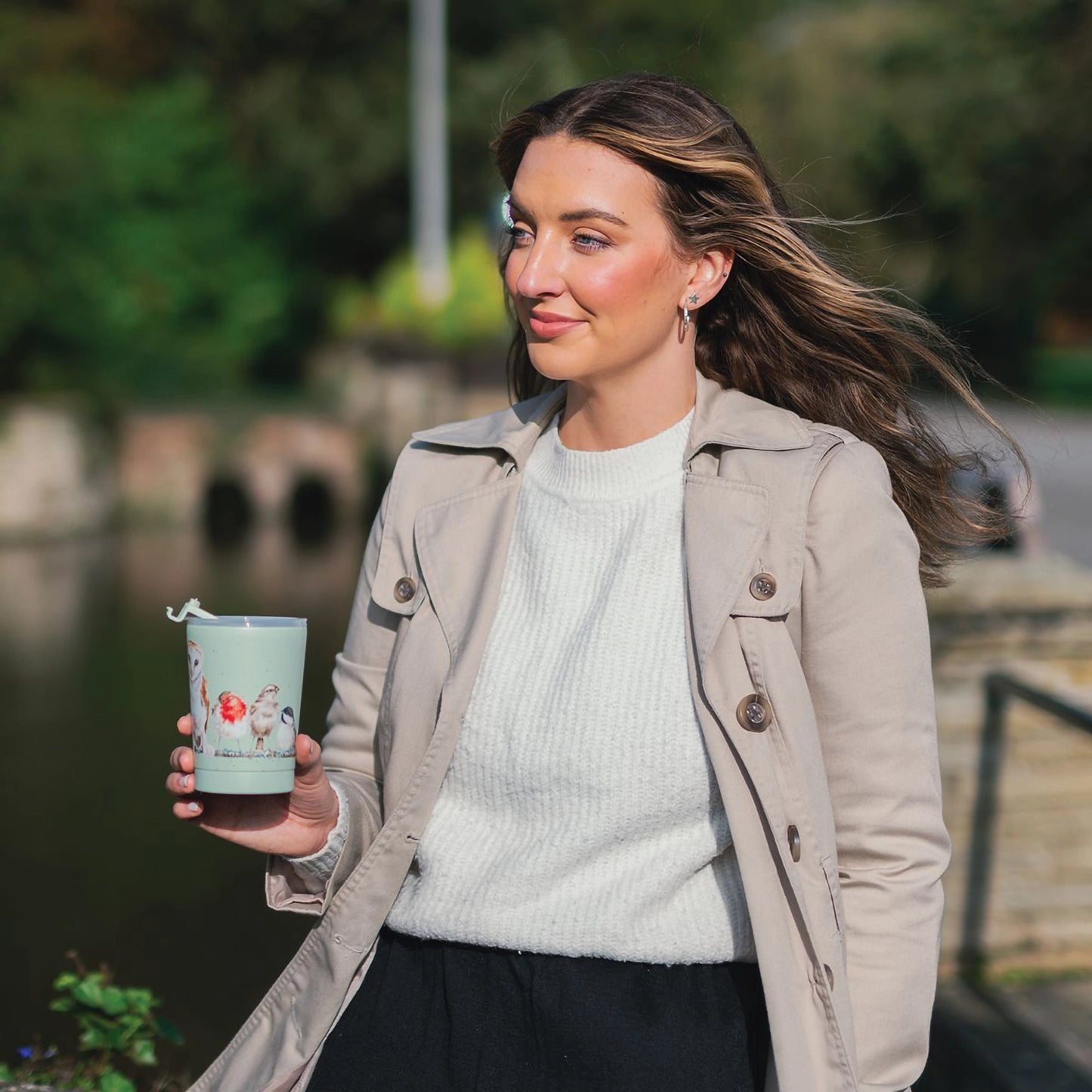 Model holding green thermal mug featuring a row of different birds on a branch design
