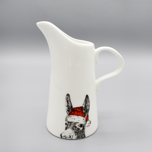 A white china jug featuring a print of a donkey wearing a red Santa hat