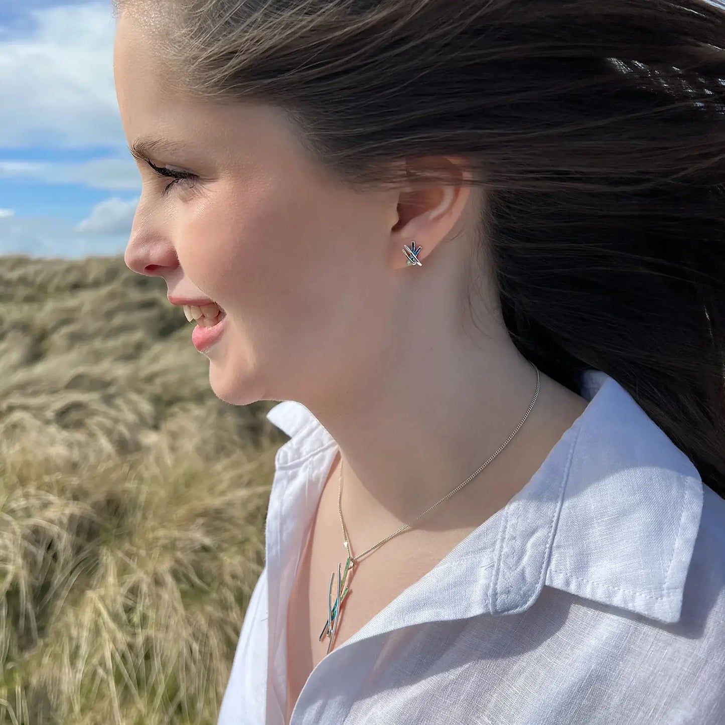 Model wearing silver earrings with four strands, two silver and two in green and blue enamel