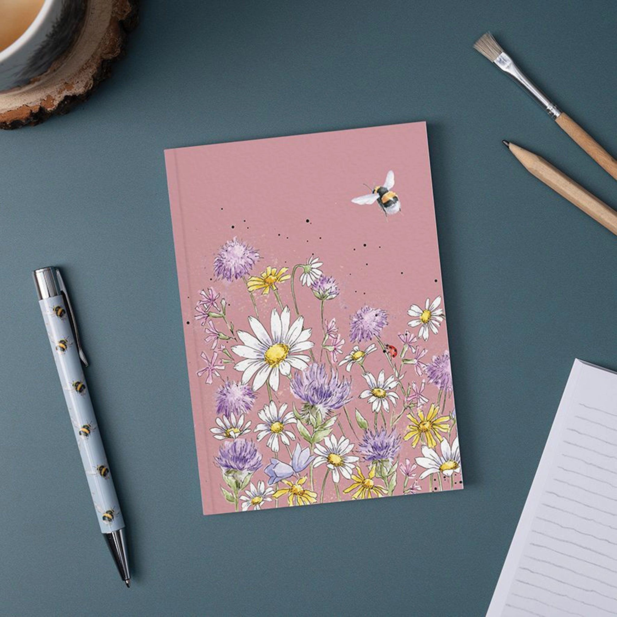 A pink paper notebook featuring an illustration of buzzing bees and wildflowers lifestyle