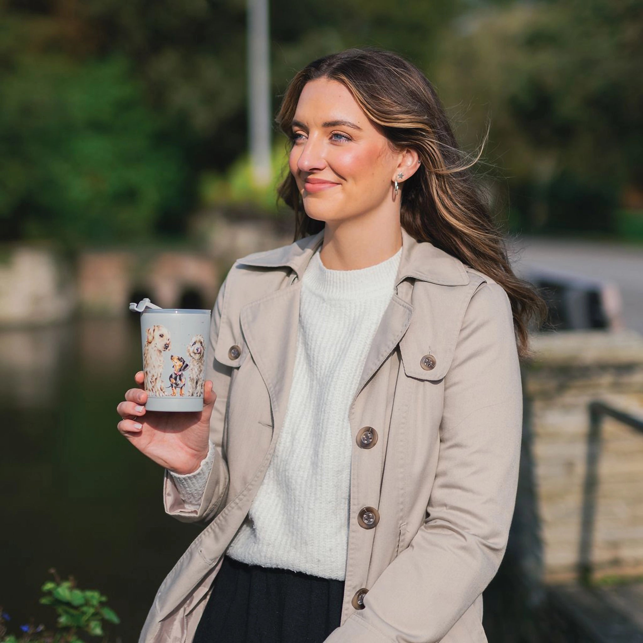 Model holding a grey travel cup featuring illustrations of different dog breeds