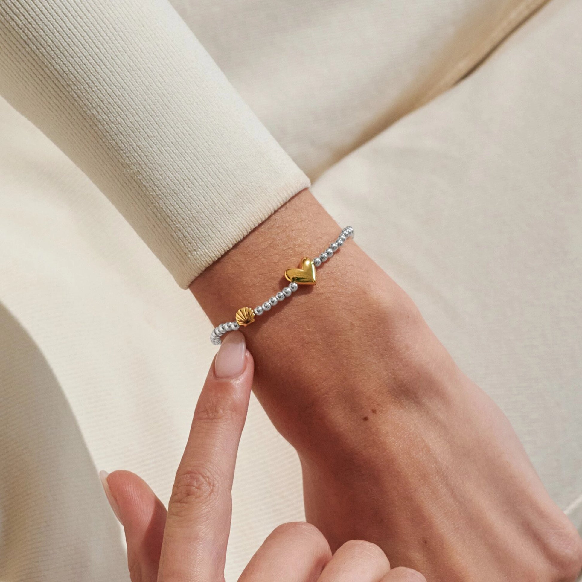 Model wearing silver beaded birth month bracelet for August with gold heart and seashell charms