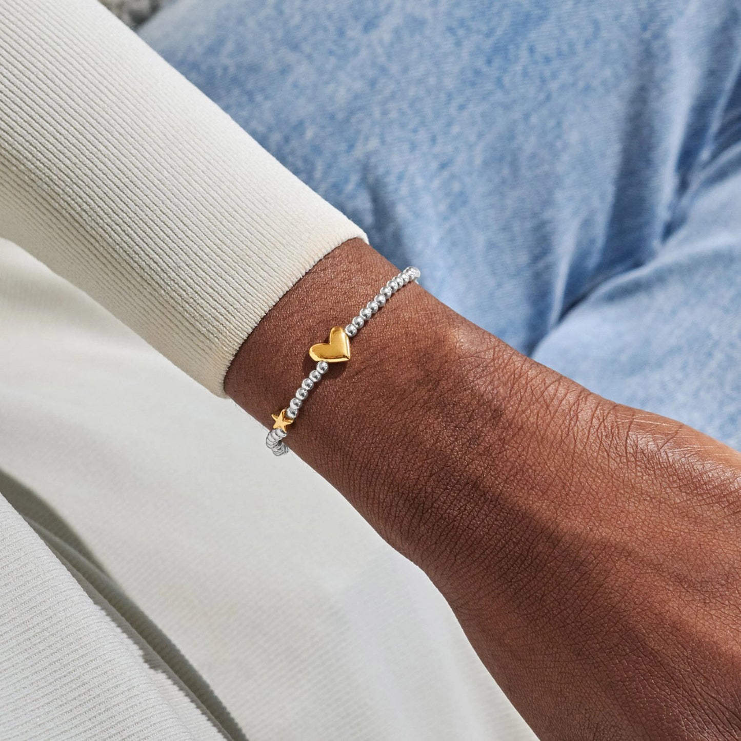 Model wearing silver beaded bracelet with a gold heart and star charm