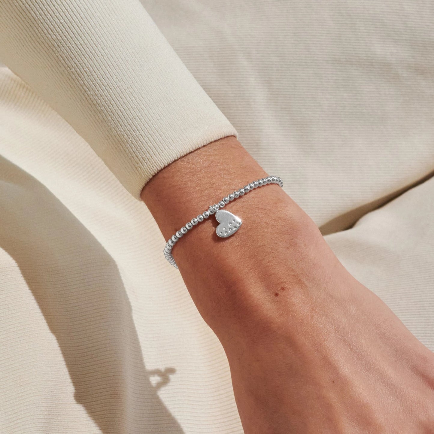 Model wearing silver stretch beaded bracelet with heart shaped charm set with a constellation of CZ stones
