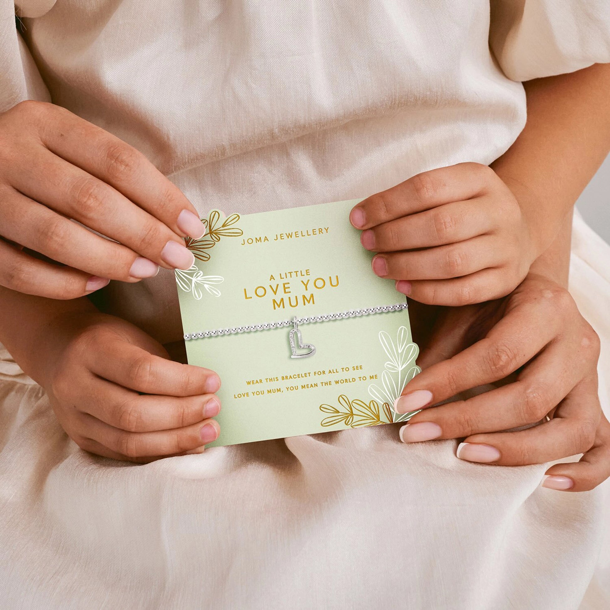 Silver beaded bracelet with CZ set open heart charm on green card held by mother and child