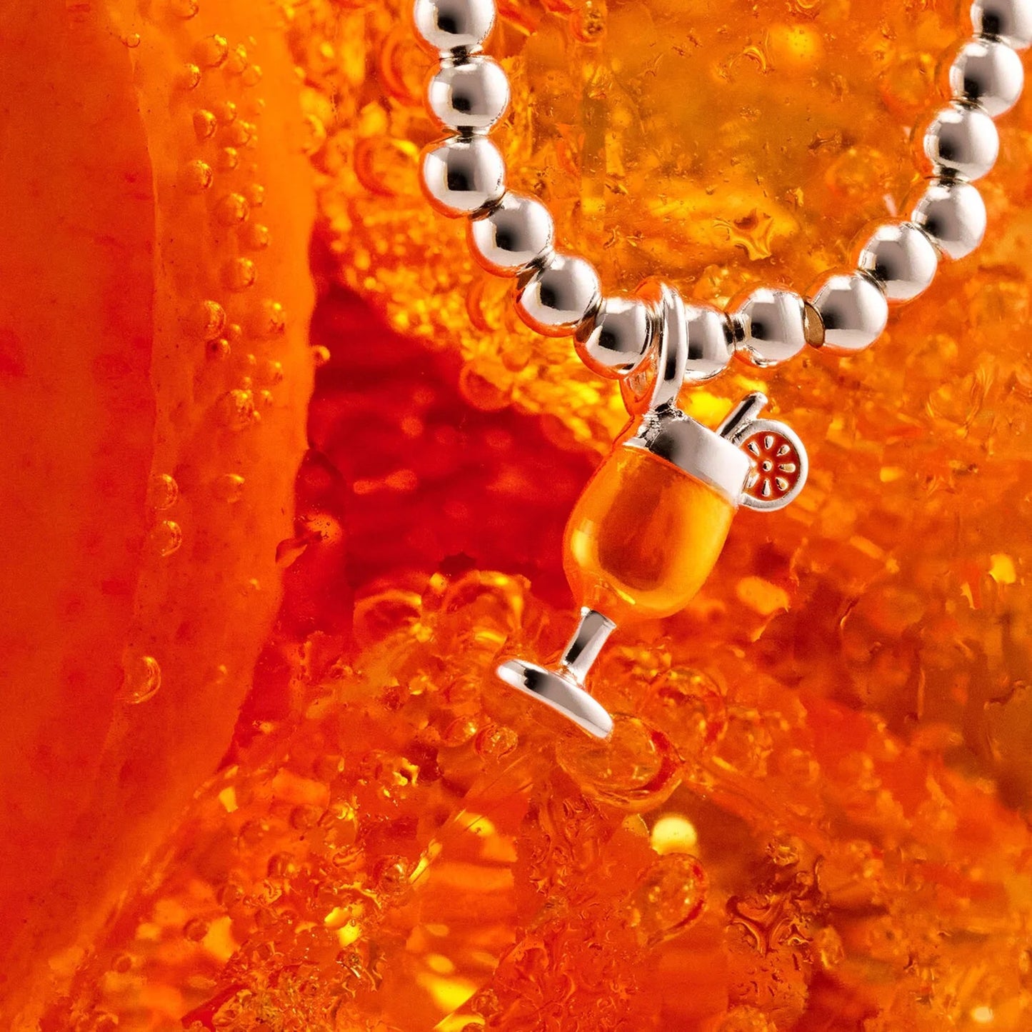 Silver beaded stretch bracelet with orange enamel cocktail drink charm on cocktail background