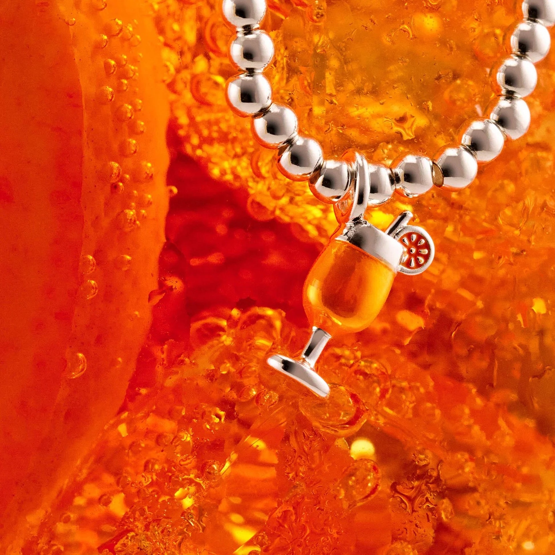 Silver beaded stretch bracelet with orange enamel cocktail drink charm on cocktail background