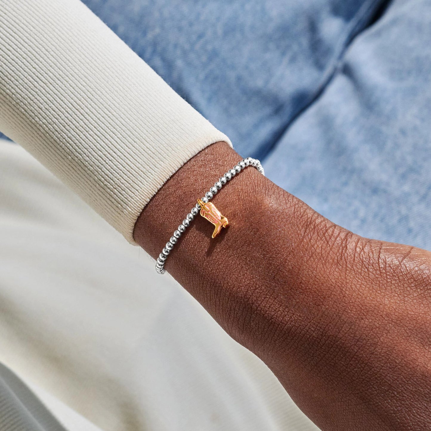 Model wearing silver beaded bracelet with gold cowgirl boot charm in gold and pink enamel