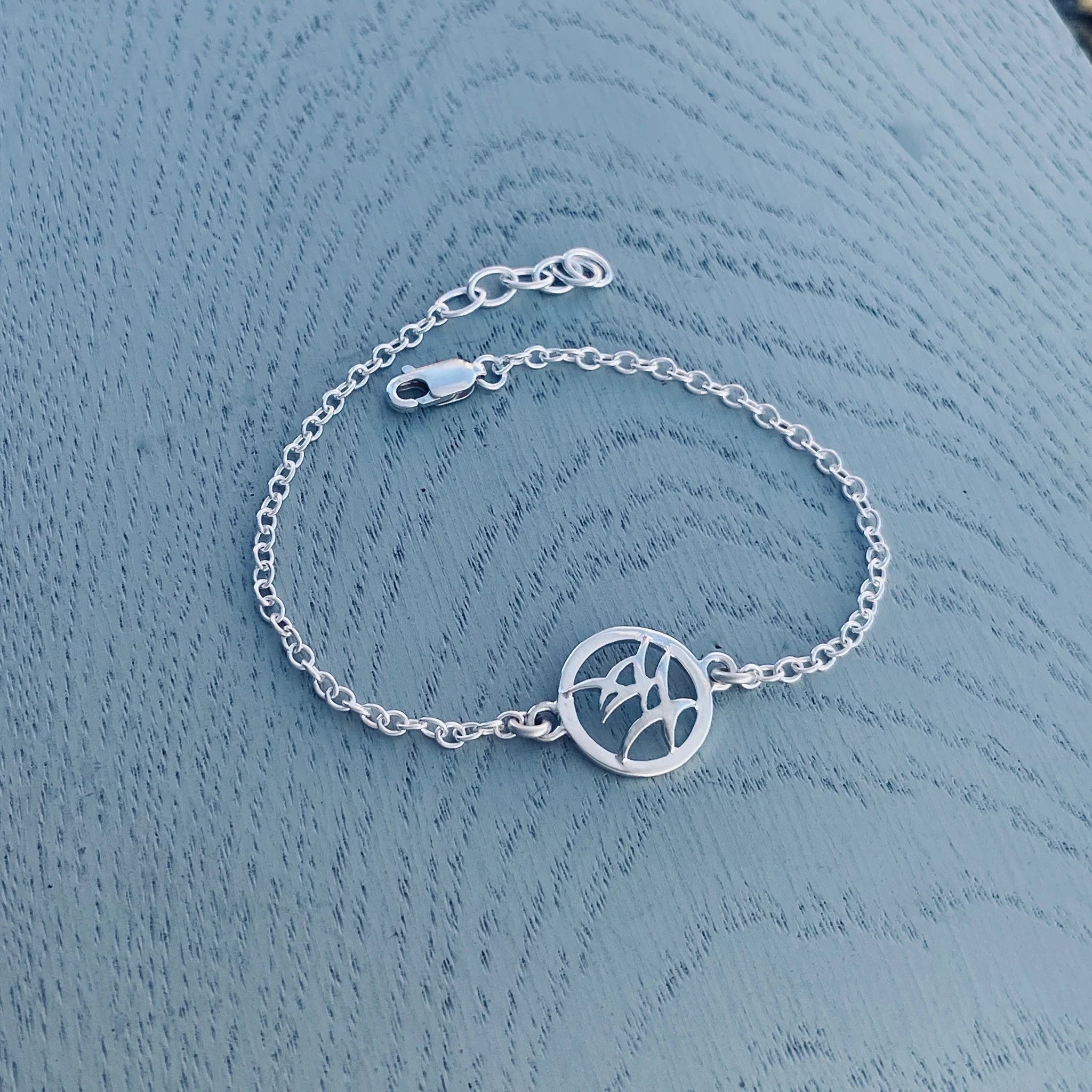 A silver chain link bracelet with a round pendant featuring a flock of birds