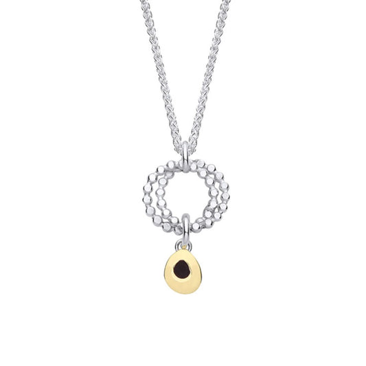 A silver pendant featuring two rings of circles and a dangling gold teardrop  