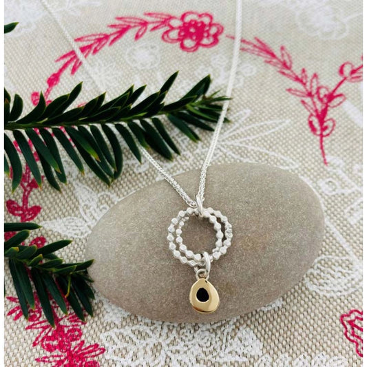 Lifestyle image of silver pendant featuring two rings of circles and a dangling gold teardrop