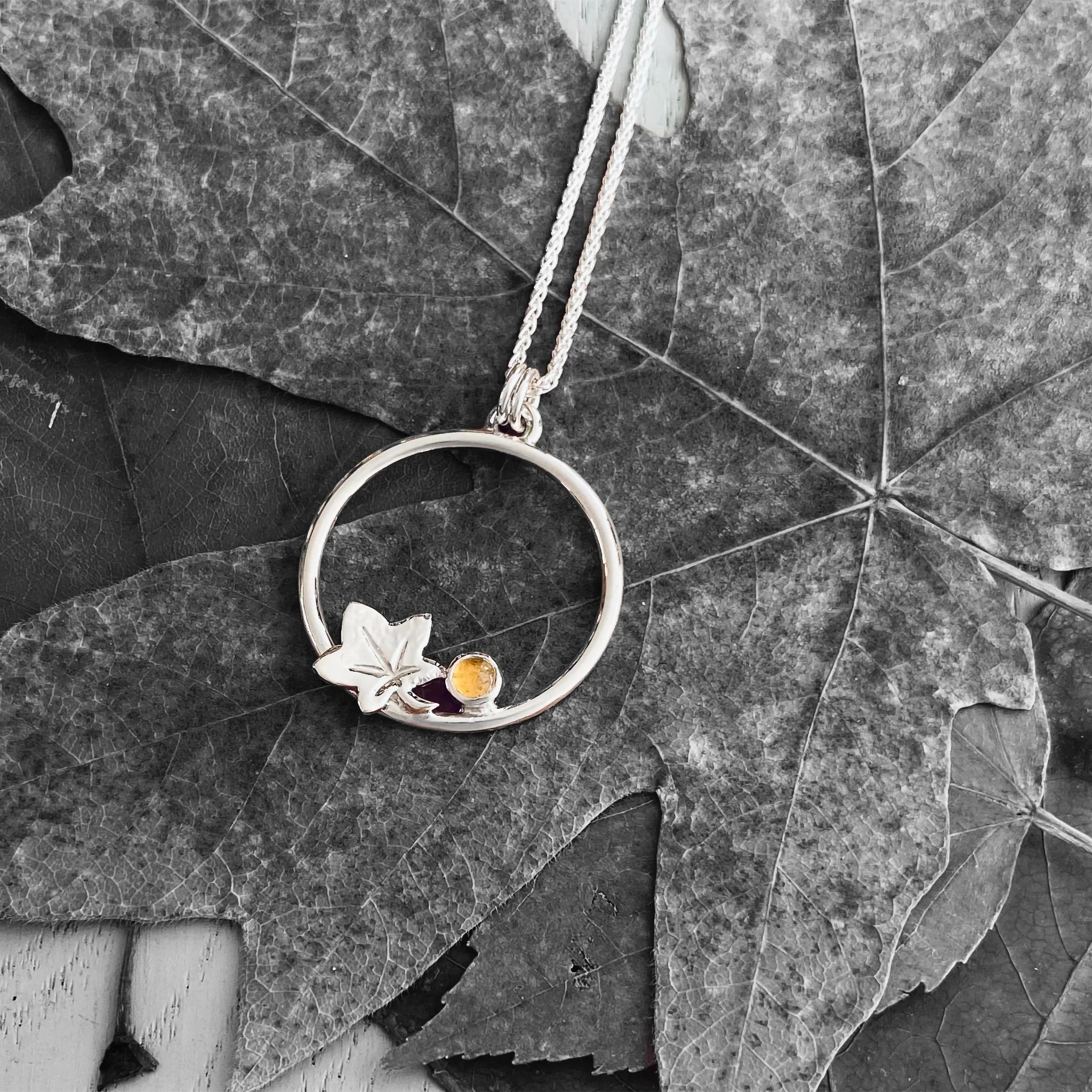 A silver loop shaped pendant with a silver autumn leaf and round citrine stone