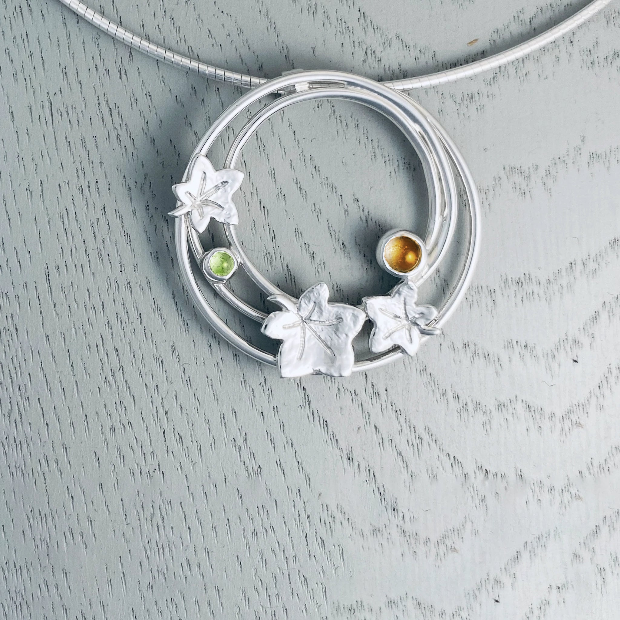 Silver necklet featuring a large round pendant with three autumn leaves and a citrine and peridot stone