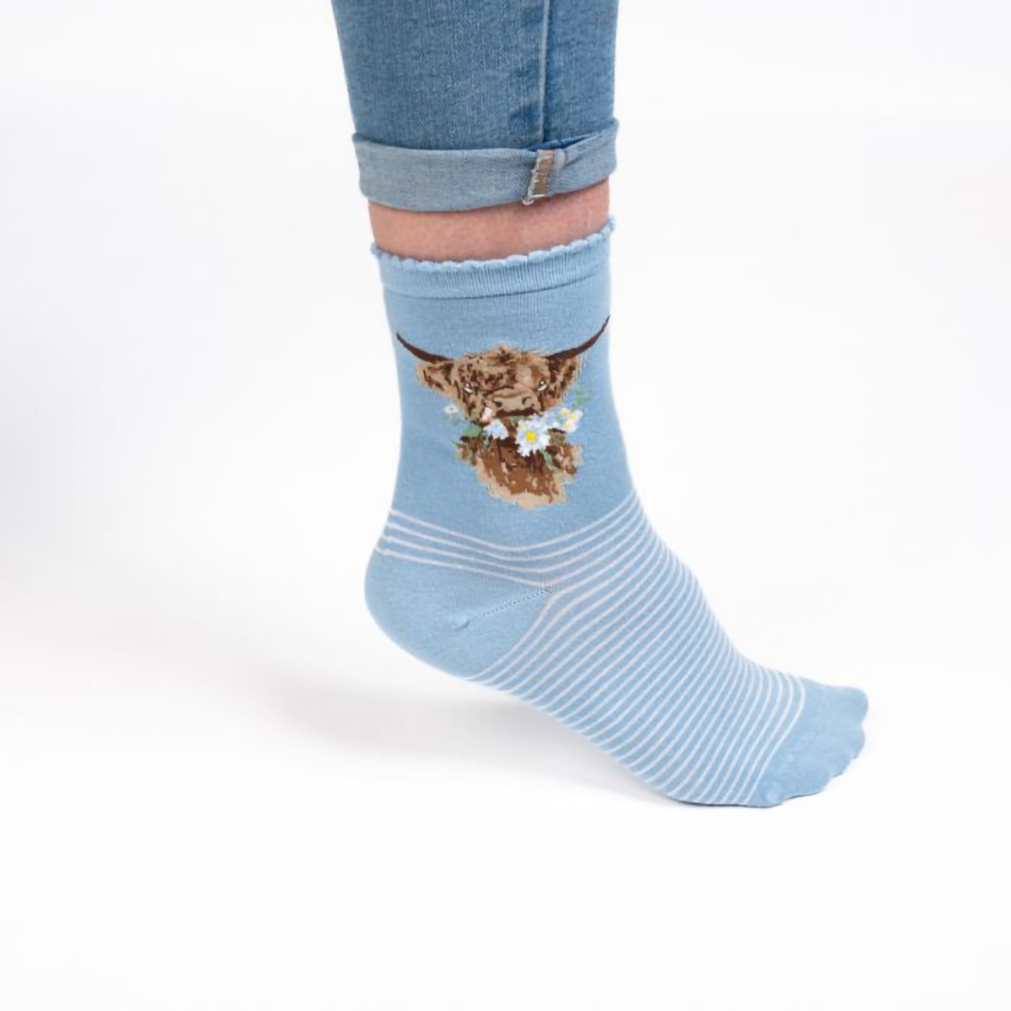 Model wearing a pair of light blue socks with a highland cow picture and white stripes and small ruffled tops