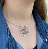 Model wearing a round necklet featuring bees in tall grass and peridot and blue topaz stones