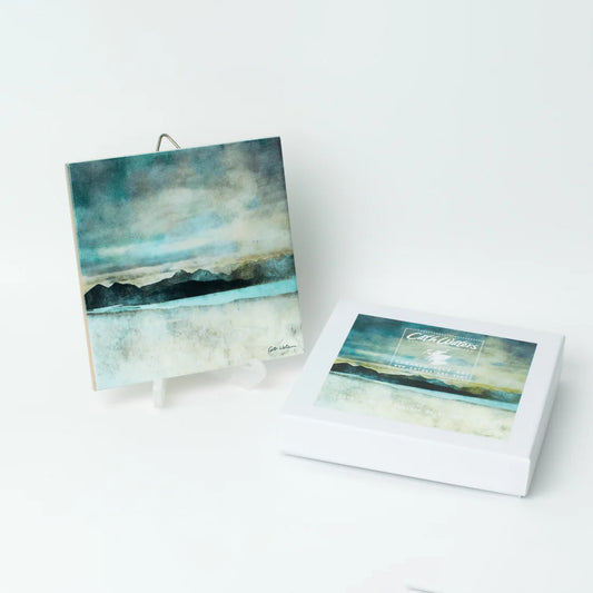 A ceramic tile featuring a landscape painting by Cath Waters with packaging