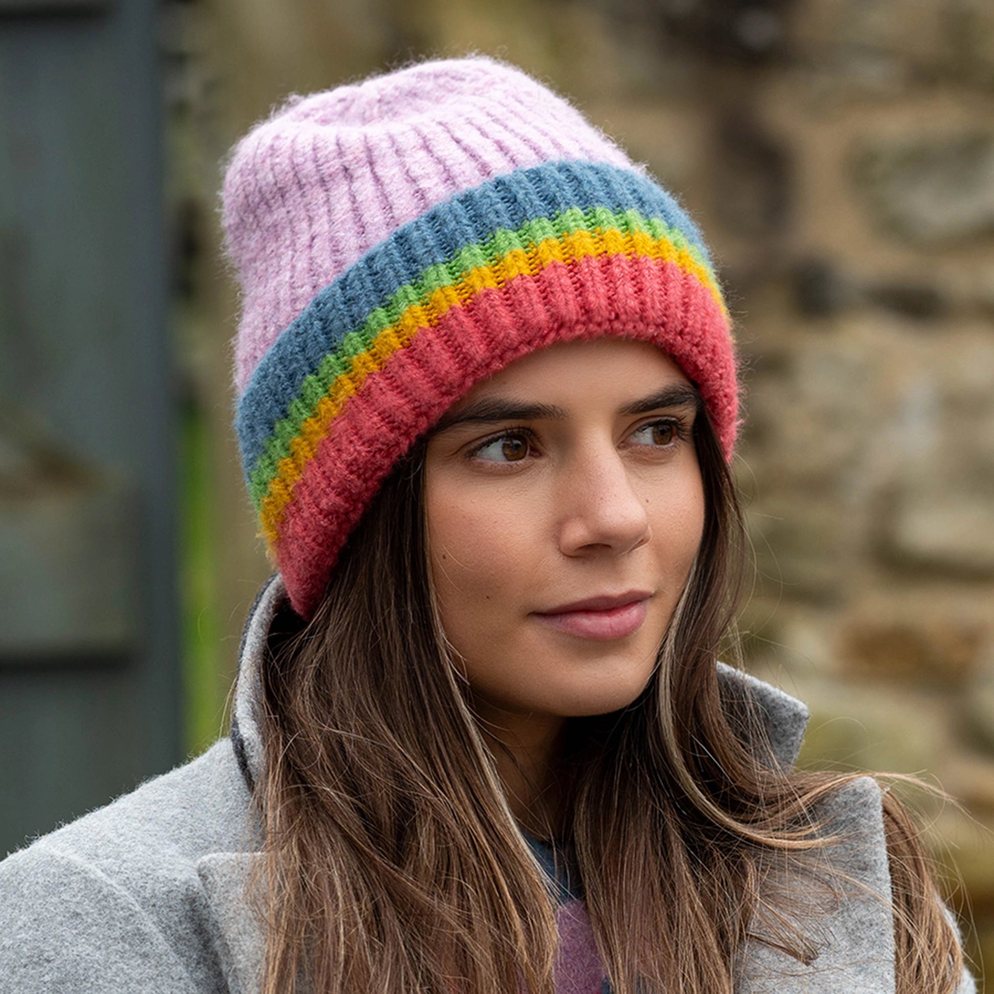 Model wearing a knitted beanie hat with lilac colour and ribbed rainbow striped turn-up
