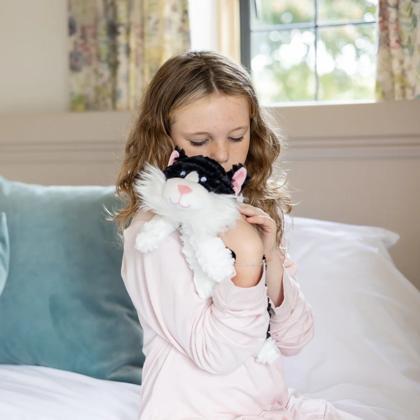 Child cuddling plush black and white cat toy with microwavable flax-seed head bag insert