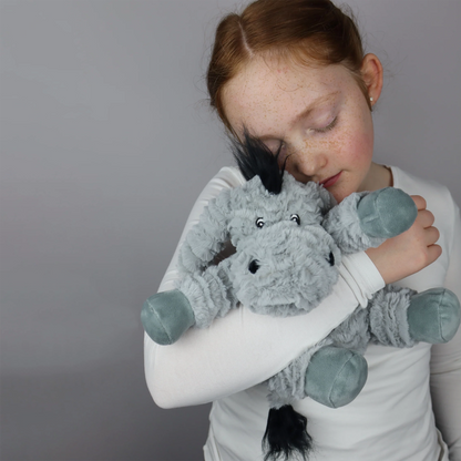 Child holding plush donkey toy in grey with microwavable flax-seed head bag insert