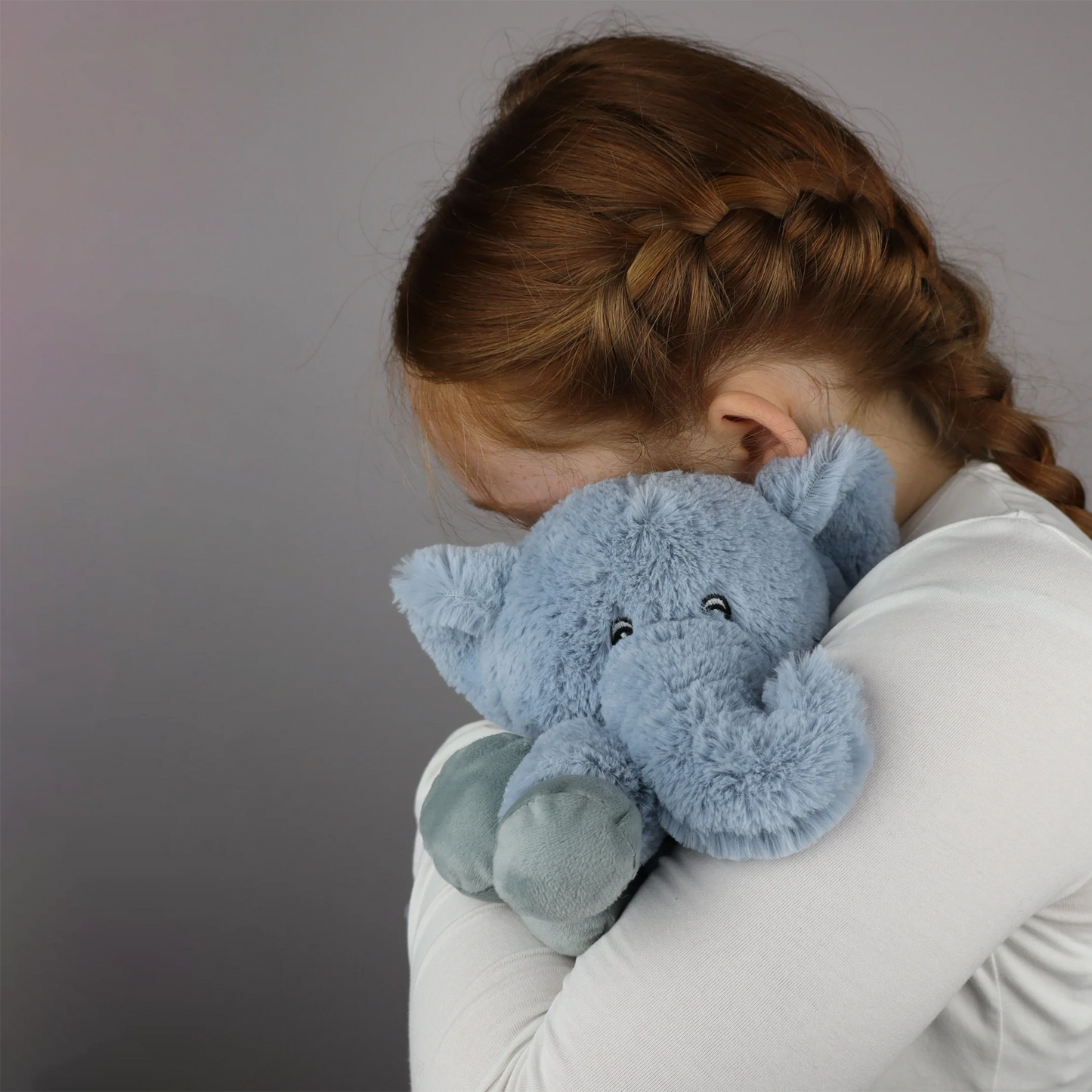 Child cuddling plush blue elephant toy with microwavable flax-seed head bag insert